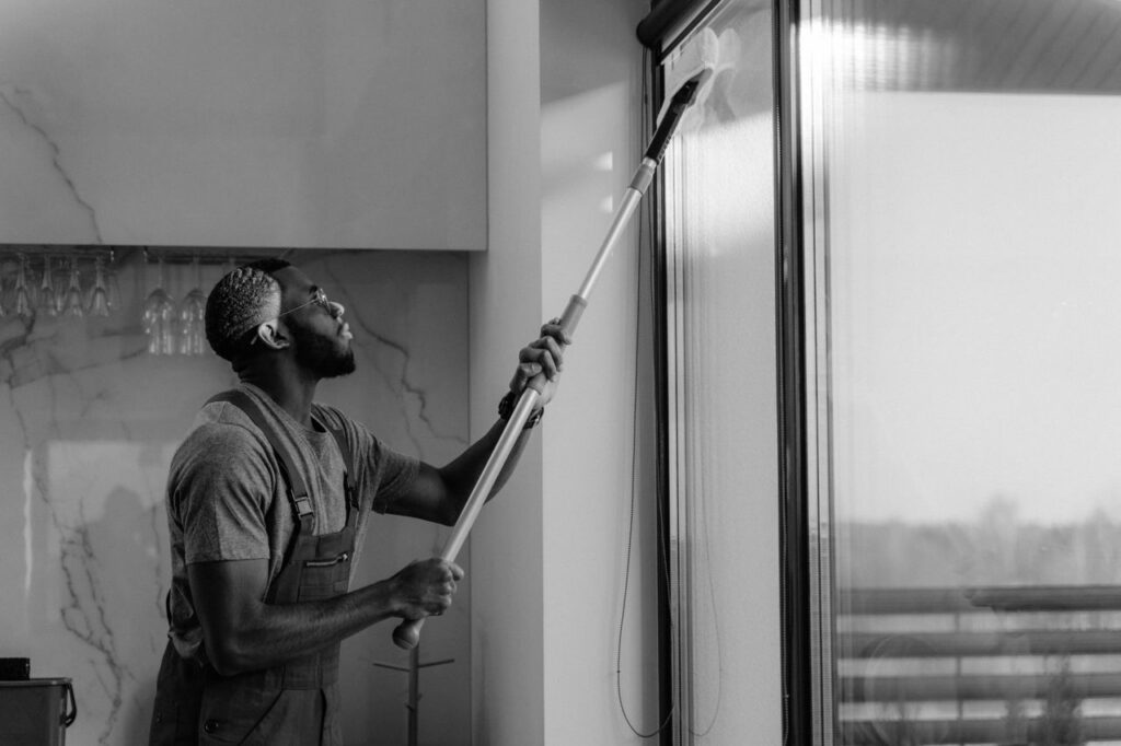 Mastering the First Impression: Your intriguing post title goes here A man cleaning a glass window with a mop in grayscale, showcasing professional work.